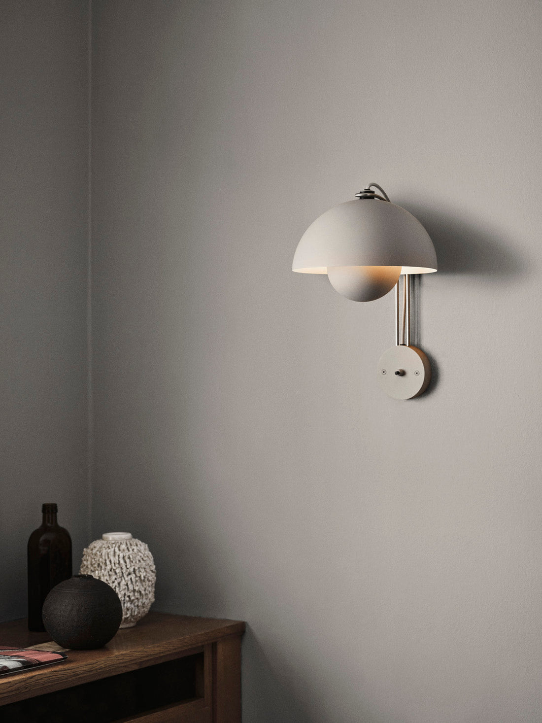 Flowerpot VP8 wall lamp by &Tradition mounted beside a bed, casting warm ambient light.