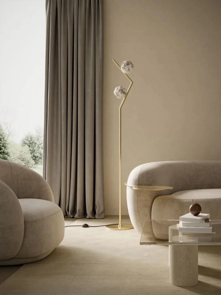 Elegant neutral living room with curved cream armchairs and sofa, sculptural brass floor lamp, floor-to-ceiling curtains, and minimalist stone coffee table.