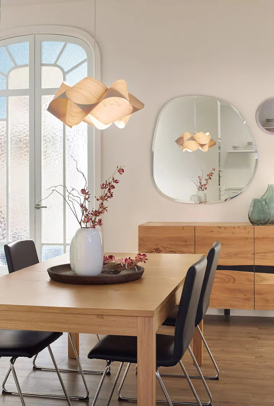 Modern dining room with light wood table and sideboard, black chairs, sculptural wooden pendant light, arched frosted glass door, and minimalist wall mirror.
