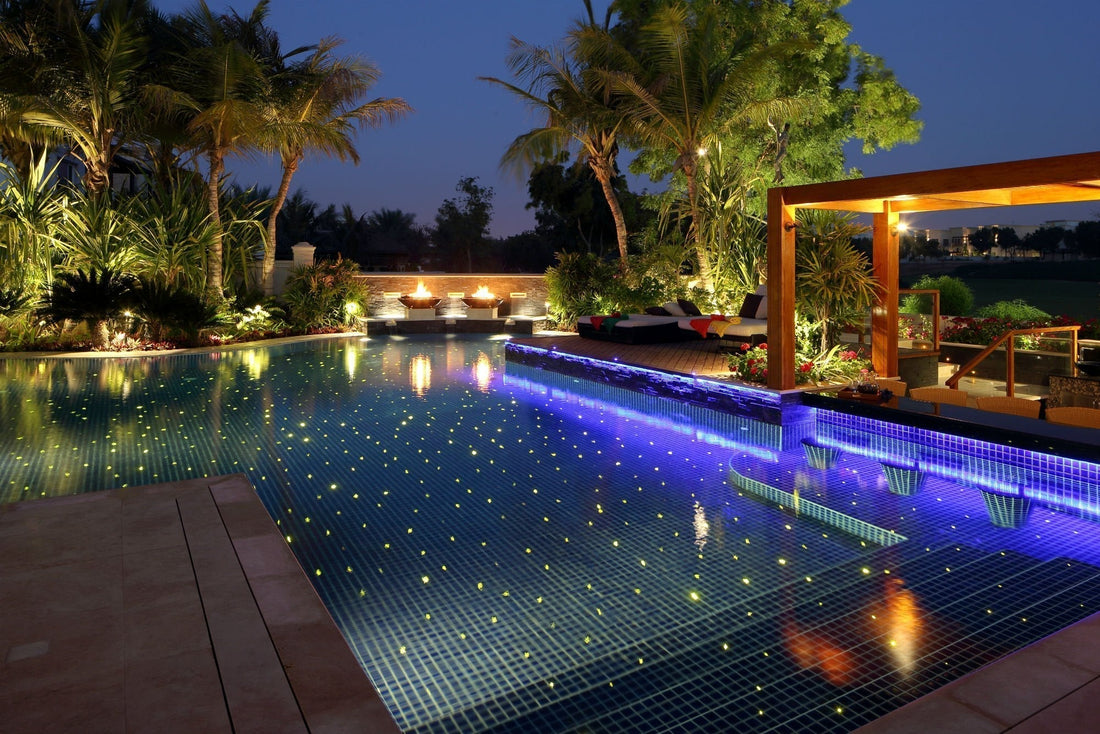 Luxury swimming pool illuminated with underwater LED lights creating a resort-style glow at night with landscaped outdoor lighting.