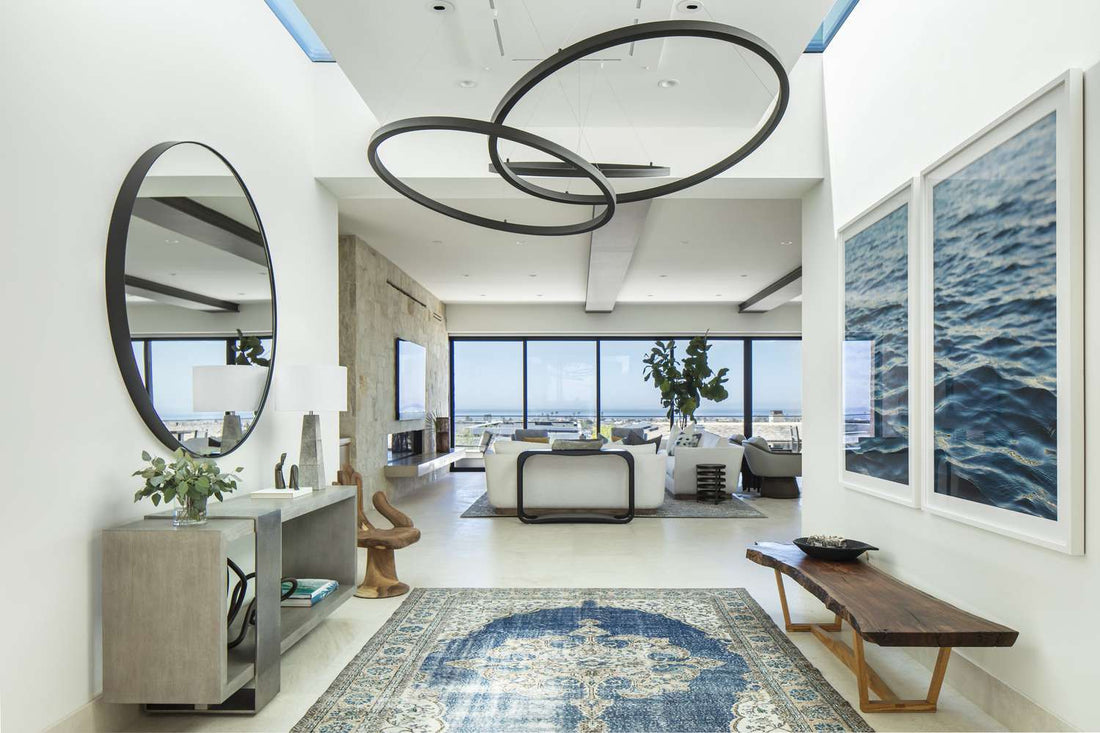 Stylish living room with large mirror reflecting hanging pendant lights, wall lamps, and natural sunlight to create a bright and luxurious interior.