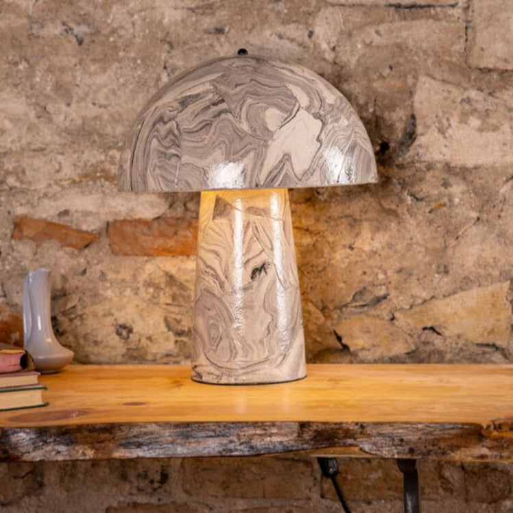 Decorative table lamp with a stone-like texture on a wooden table against a stone wall.