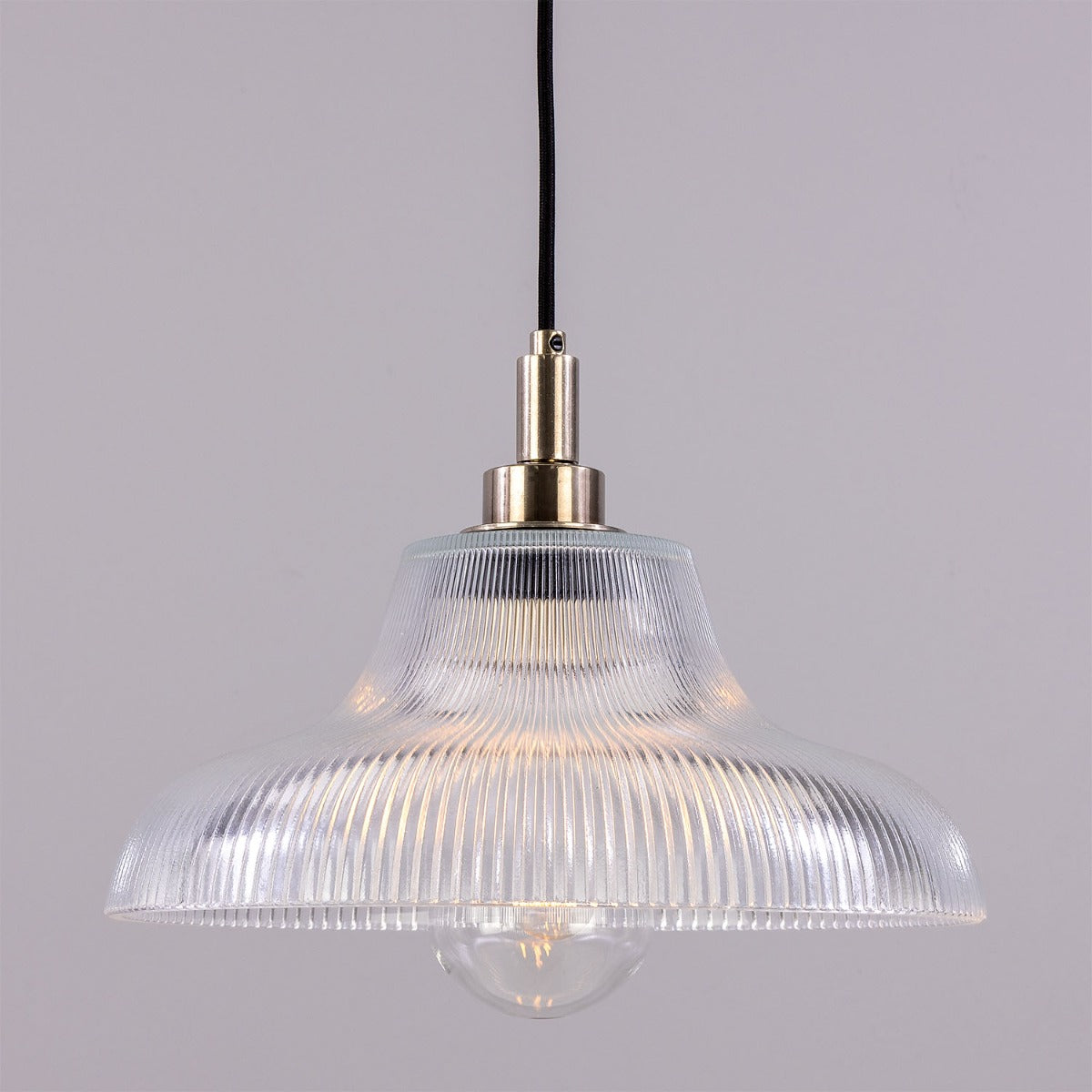 Clear ribbed pendant light with brass fitting on a gray background