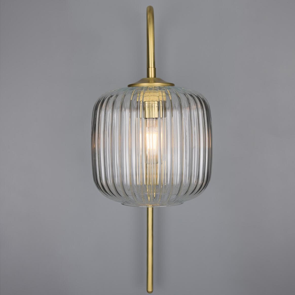 Decorative wall light fixture with ribbed glass shade and gold finish on a gray background