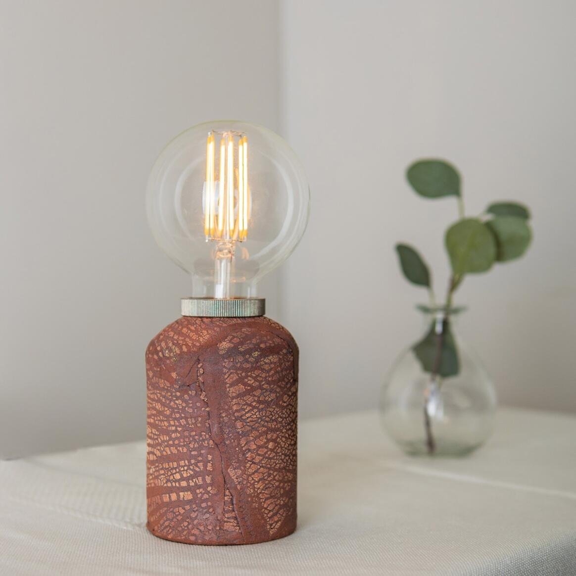 Ceramic table lamp with a textured brown base and clear glass shade on a white surface.