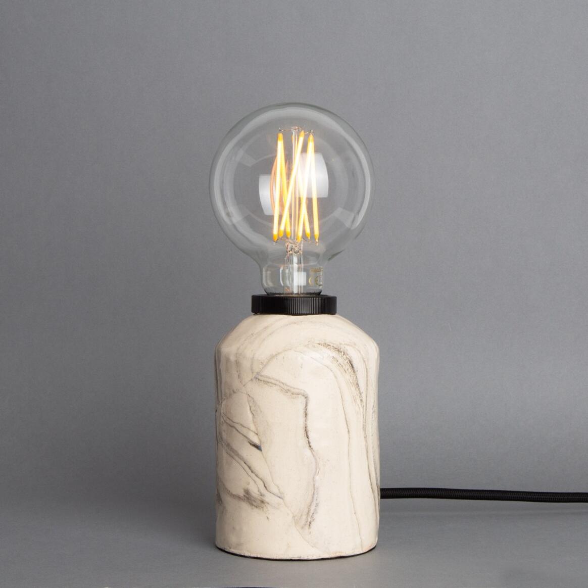 Table lamp with a marble base and illuminated bulb on a gray background