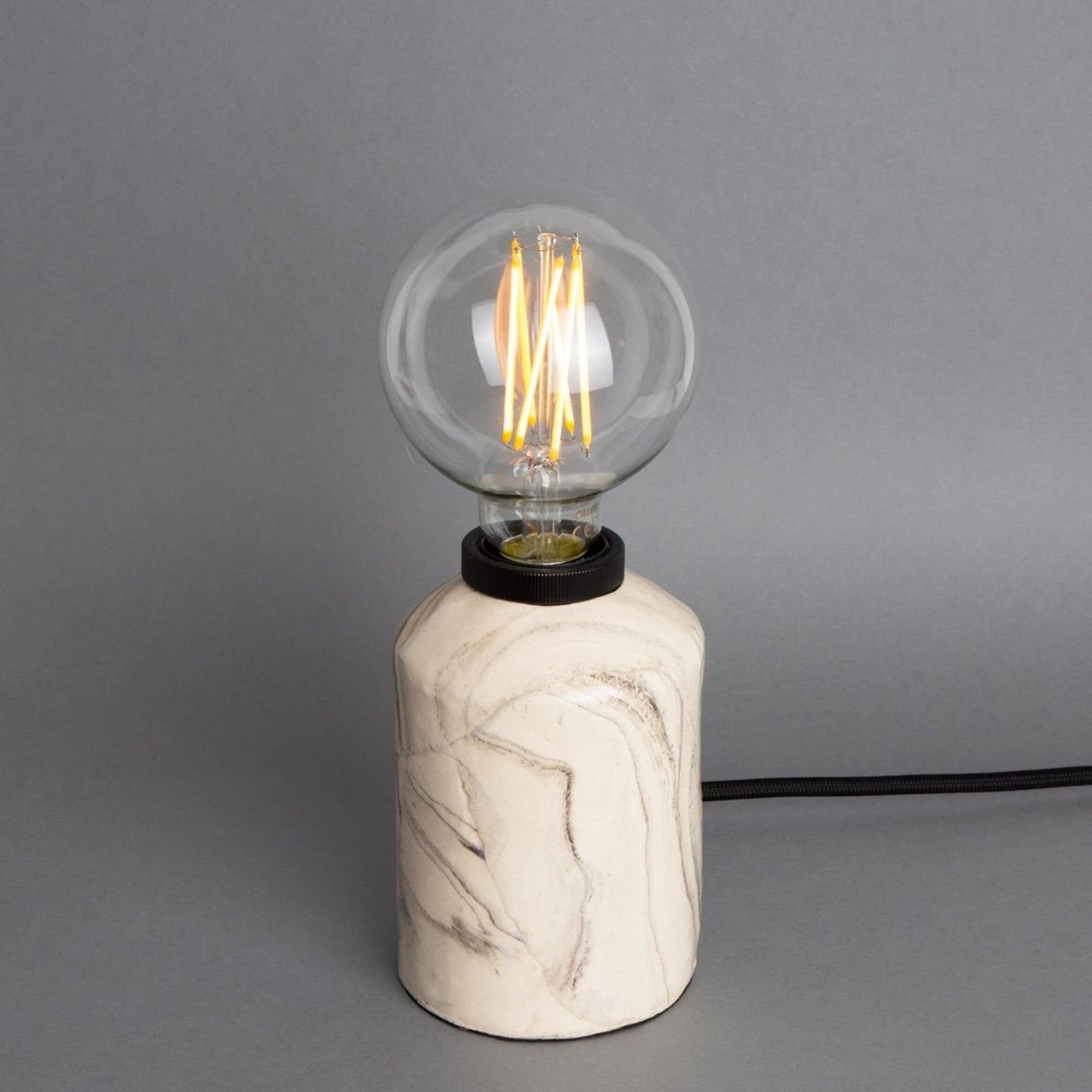 Marble-textured lamp with a lit bulb on a gray background