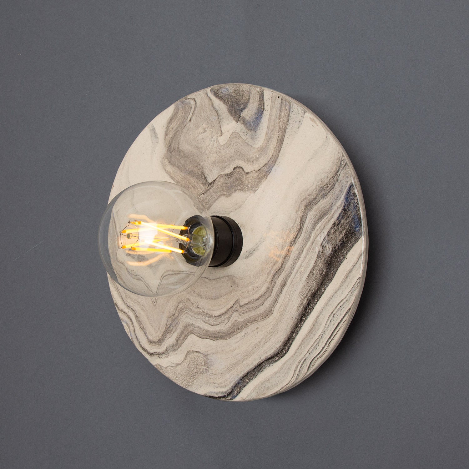Round wall light fixture with marble-like design on a dark gray background
