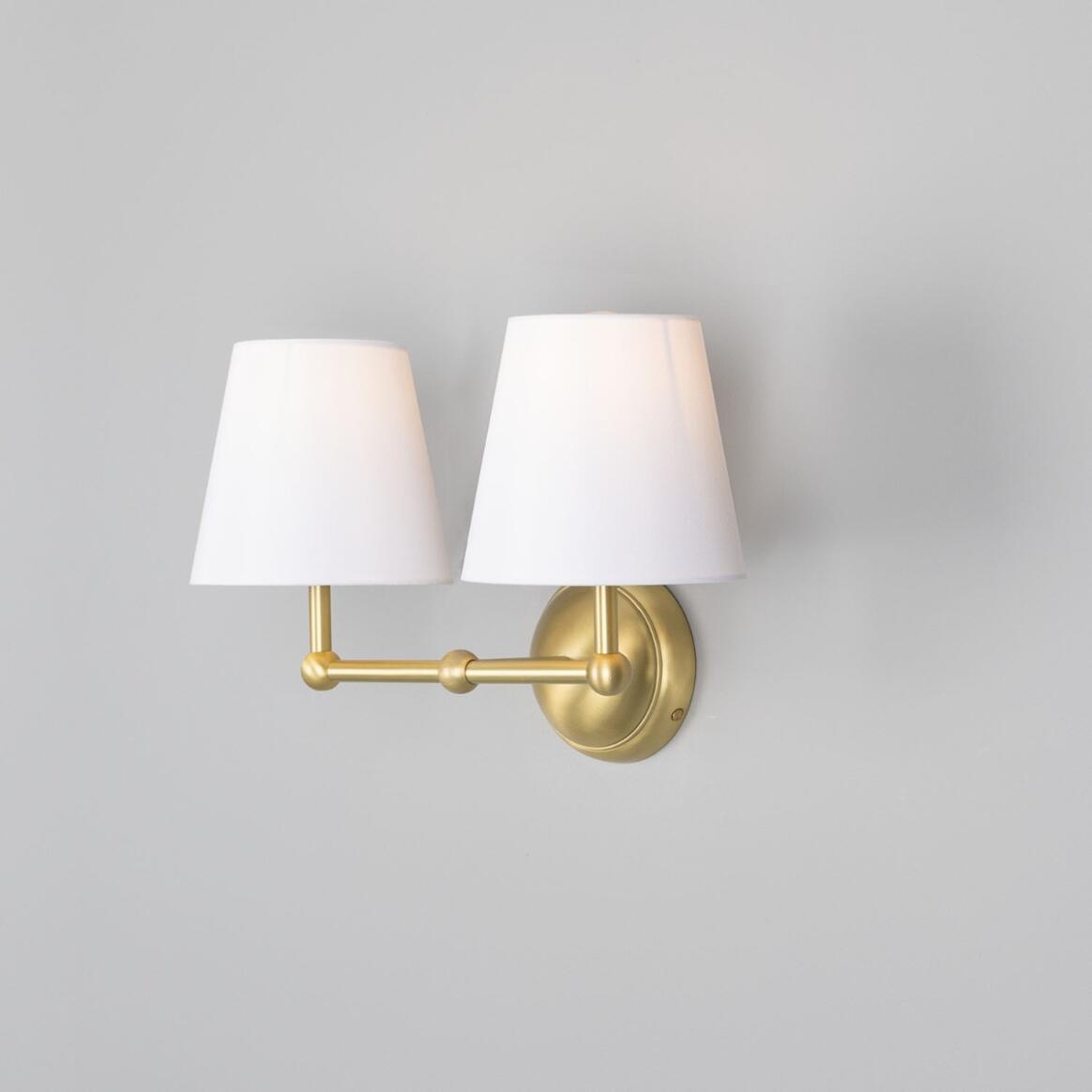 Wall-mounted lamp with two white shades and gold fixture on a gray background