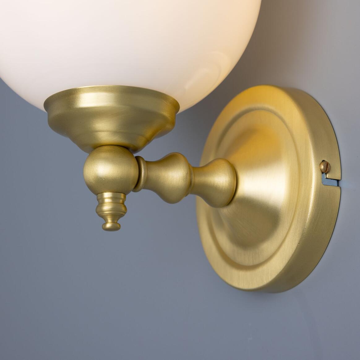 Brass wall sconce with a white glass shade on a gray background