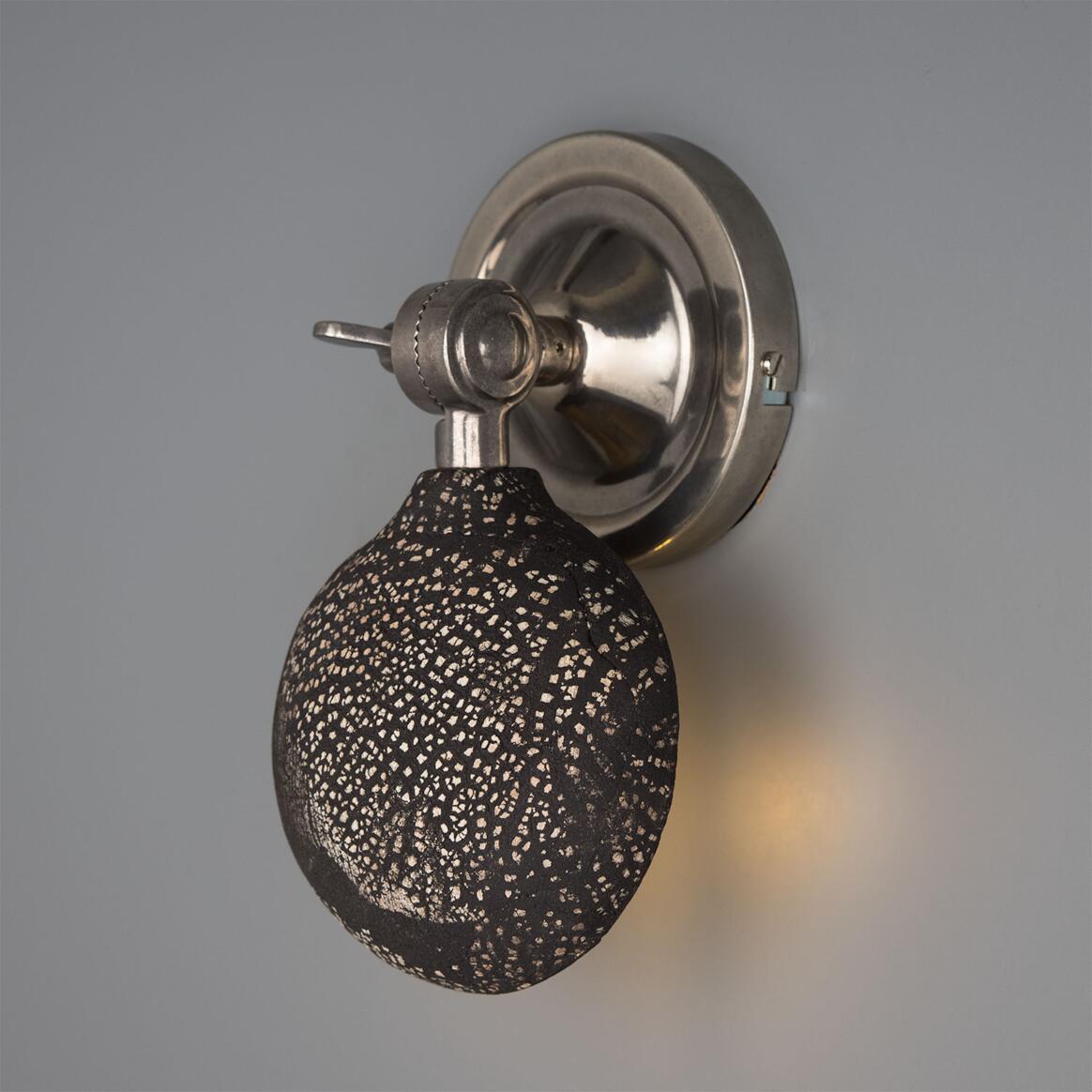 Wall-mounted light fixture with textured black bulb on a gray background