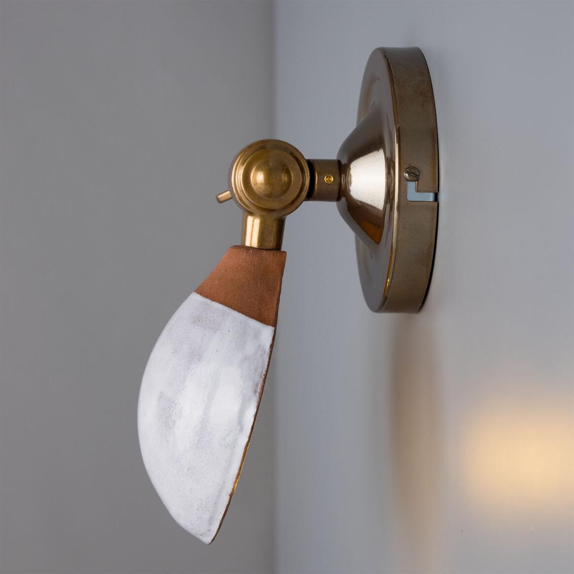 Wall-mounted light fixture with brass and white design on a gray wall.