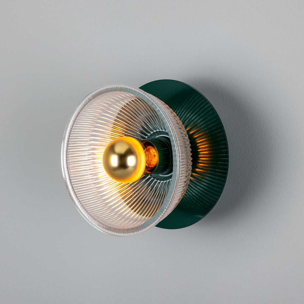 Wall-mounted light fixture with green base and gold bulb on a gray background
