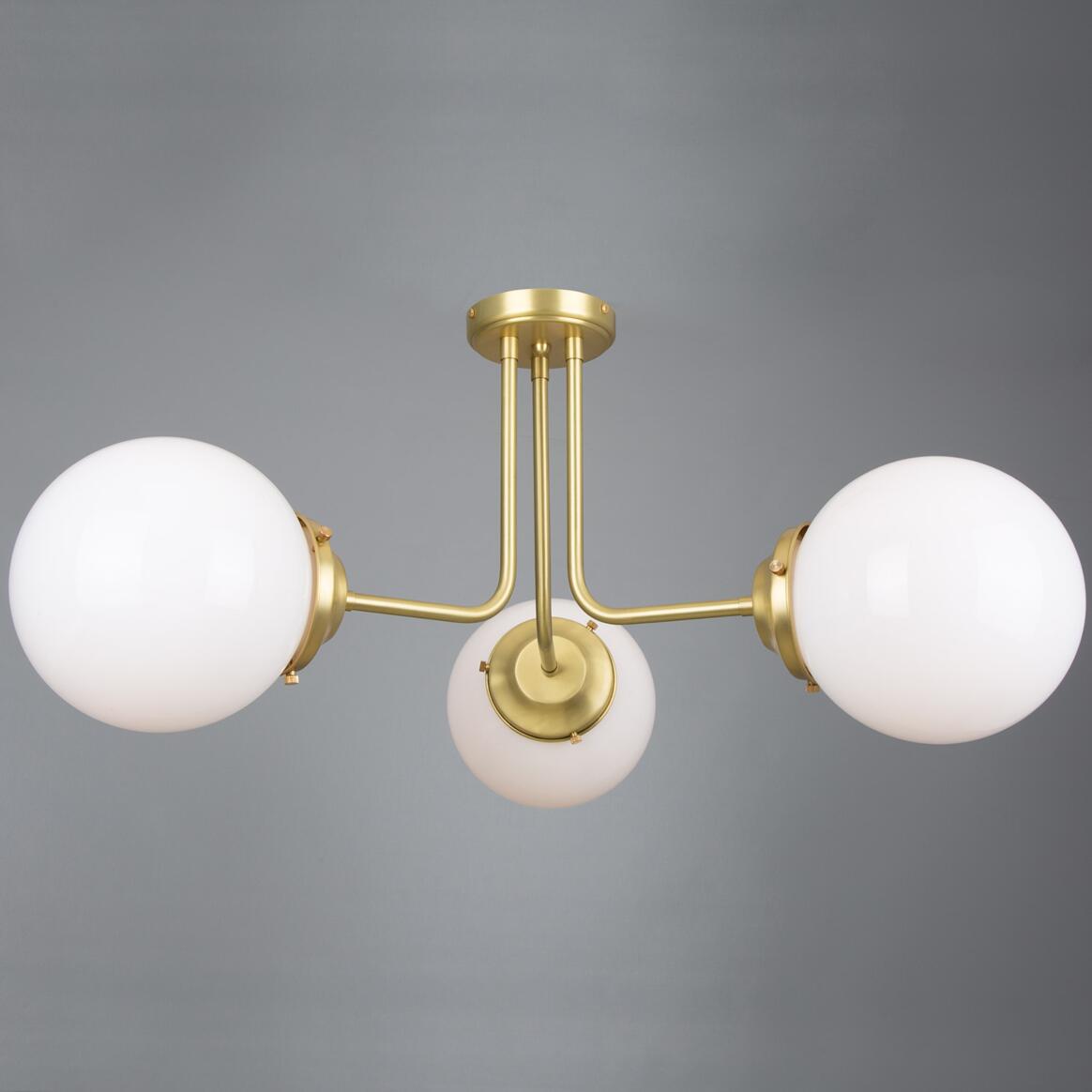 Modern ceiling light fixture with three white glass globes and gold metal accents on a gray background