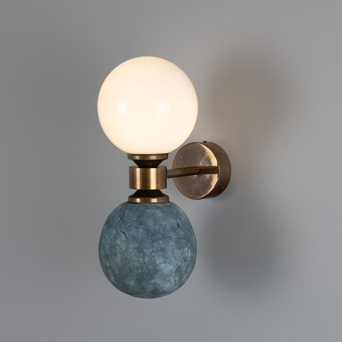 Wall sconce with a glass globe and textured stone base on a gray background