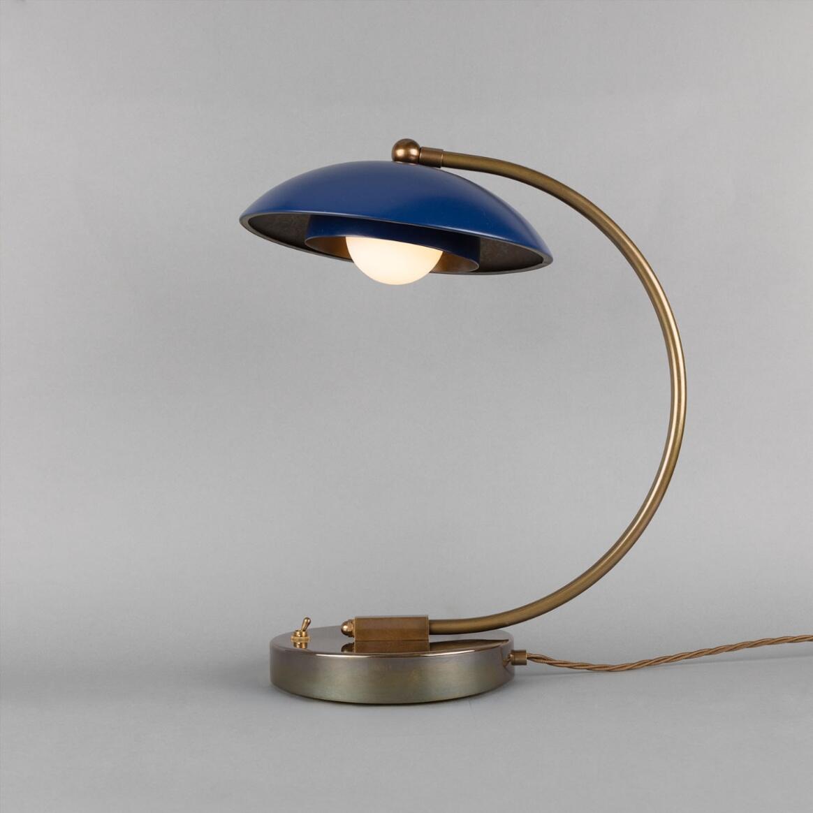 Vintage-style table lamp with blue shade and brass arm on a gray background