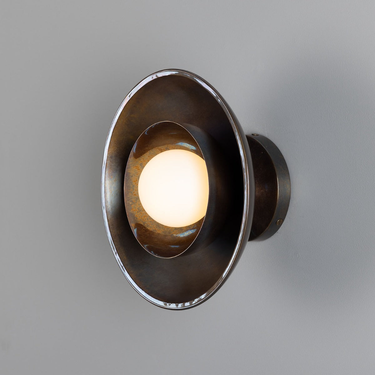 Wall-mounted light fixture with a metallic finish on a gray background