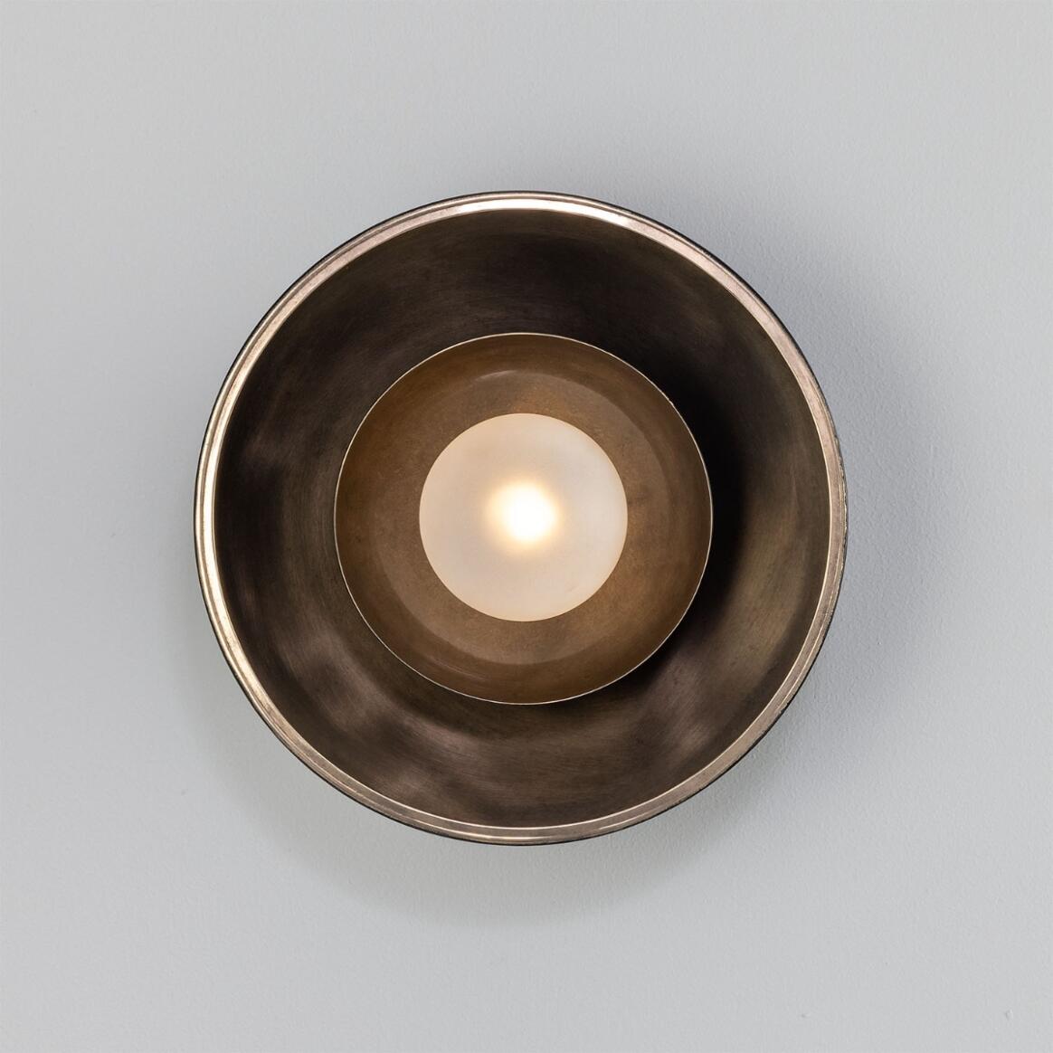 Bronze candle holder with a lit candle on a gray background