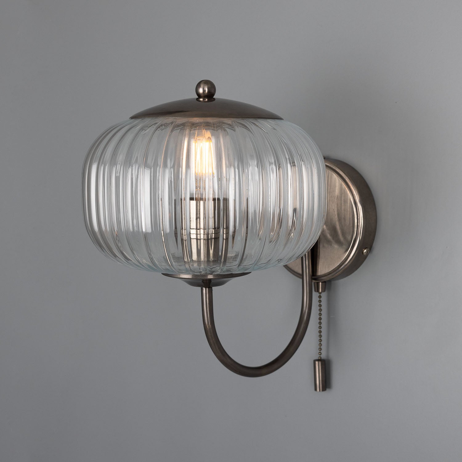 Wall-mounted light fixture with glass shade on a gray background