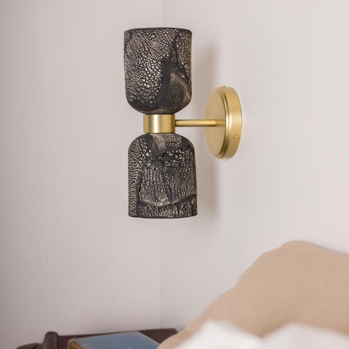 Wall-mounted lamp with textured black shade and gold fixture on a light beige wall.