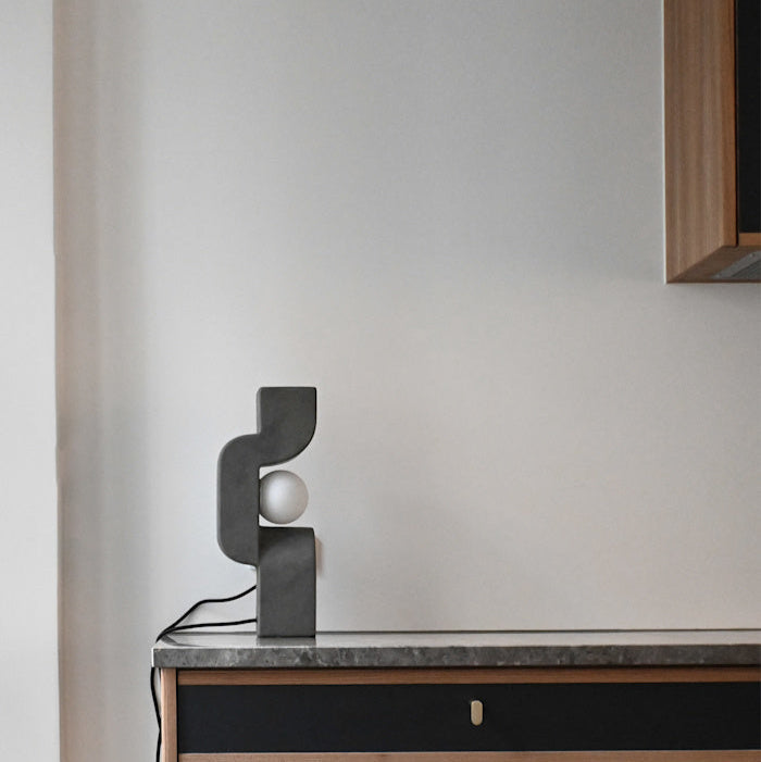 Sitting Man Table Lamp by 101 Copenhagen featuring a sculpted figure seated with an overhead light source on a minimalist table.