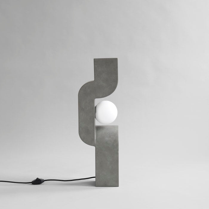Sitting Man Table Lamp by 101 Copenhagen featuring a sculpted figure seated with an overhead light source on a minimalist table.