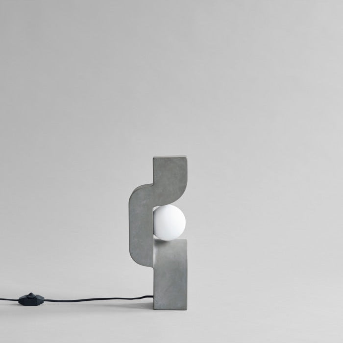 Sitting Man Table Lamp by 101 Copenhagen featuring a sculpted figure seated with an overhead light source on a minimalist table.